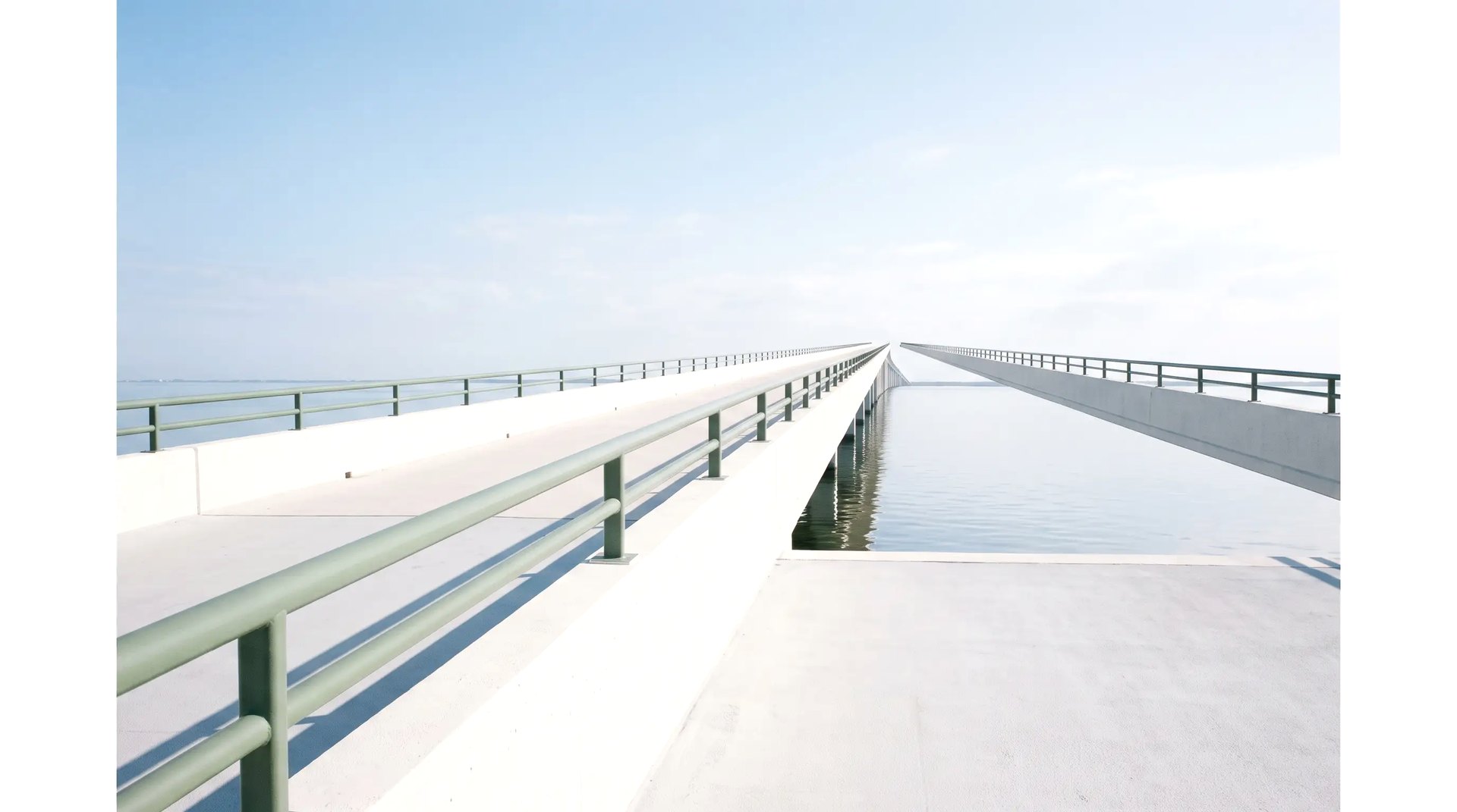 Une passerelle de béton blanc sur l’eau, une ligne verte le long de la rambarde